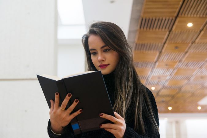 Woman standing along bookshelves and holding open book