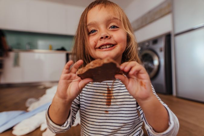 Beautiful little girl showing a chocolate she is eating with chocolate on her shirt