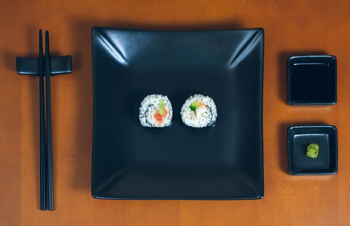 Top view of two freshly made sushi rolls on rectangular plate on table, ready to eat
