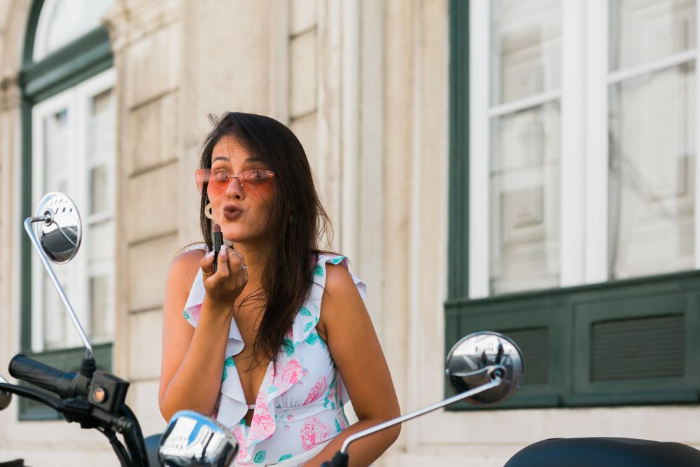 Woman putting lipstick looking at motorcycle mirror