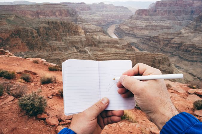Male drawing in notebook at rock