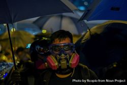 Man wearing gas mask standing under an umbrella during Hong Kong protests 5oKmG5