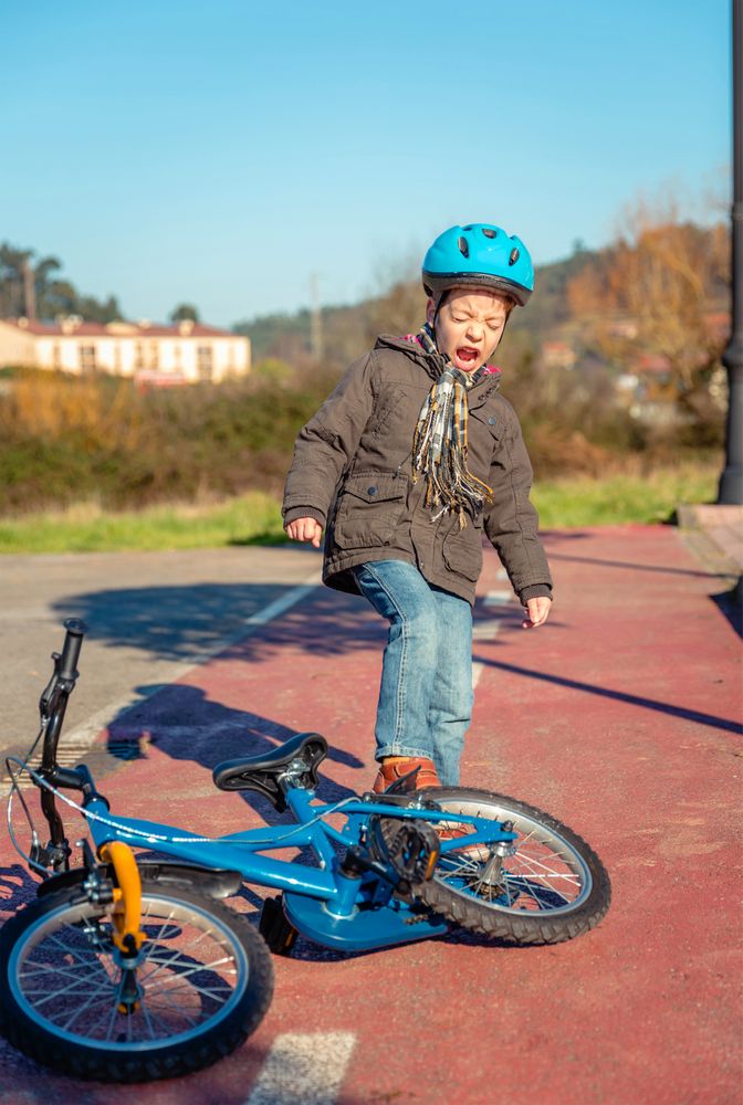 Distressed boy kicking bike in frustration after falling