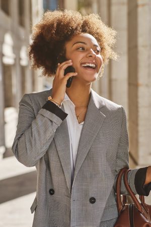 Cheerful Black woman speaking on smartphone on city s