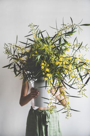 Woman holding mimosa branches in vase, her face covered