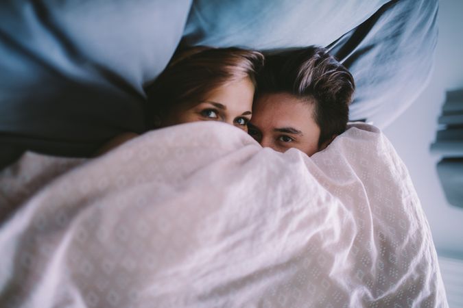 Couple lying down and peaking out from under a blanket