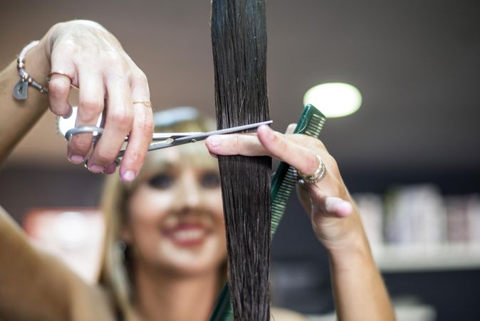 Hair stylist smiling and holding up brunette wet hair while cutting