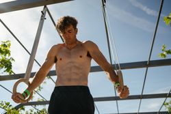 Strong young sportsman exercising with rings