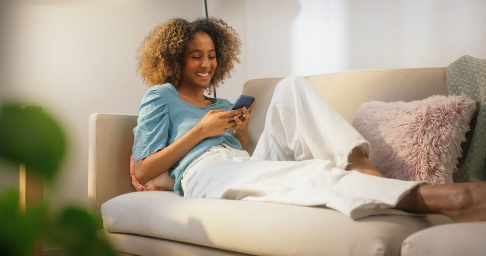 Woman with Curly Hair Enjoying her Evening in Sunny Apartment, Browzing Internet, Chatting with Friends Online