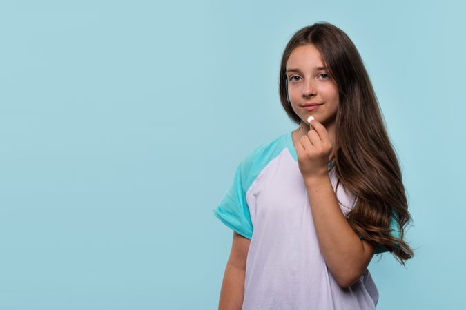 Young girl holds white pill near her mouth