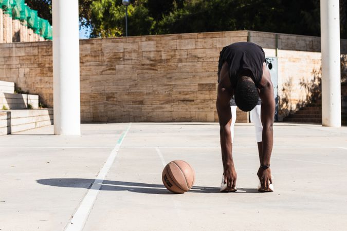 Black sportsman stretching on basketball court