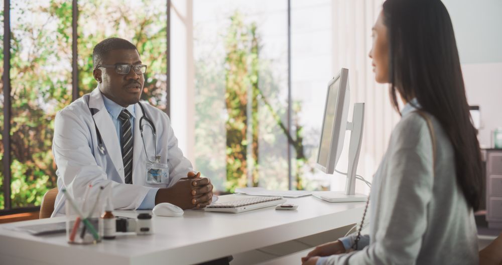 Black Doctor is Having a Conversation with an Asian Patient, Speaking with Her During Consultation in a Health Clinic.