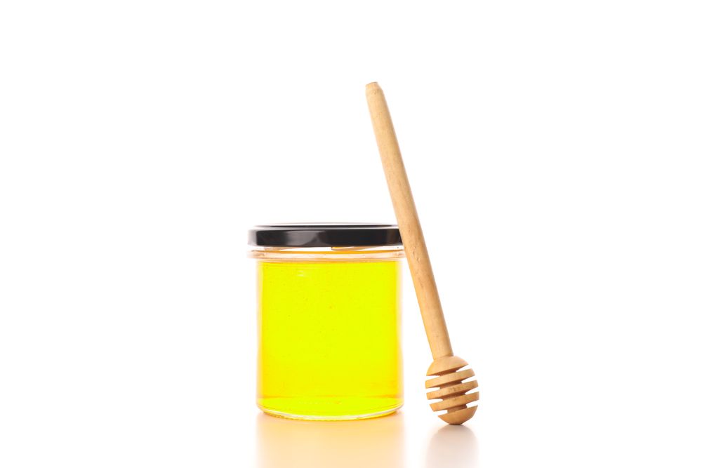 Glass jar with honey and dipper isolated on plain background