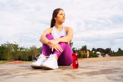 Positive sportswoman with bottle of water sitting on sports ground