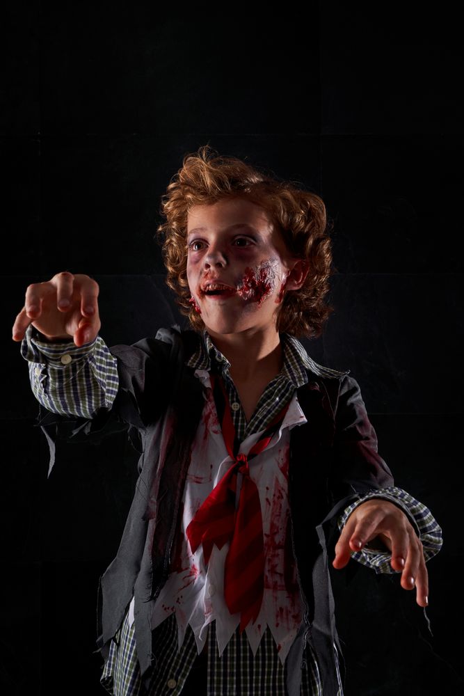Vertical photo of a child disguised as a zombie with blood and glitter with arms raised walking