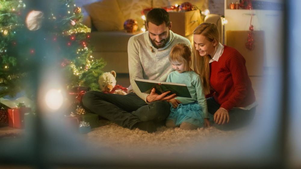 Sitting Under Christmas Three with Gifts Under It Father and Mother Read a Book to Little Daughter.
