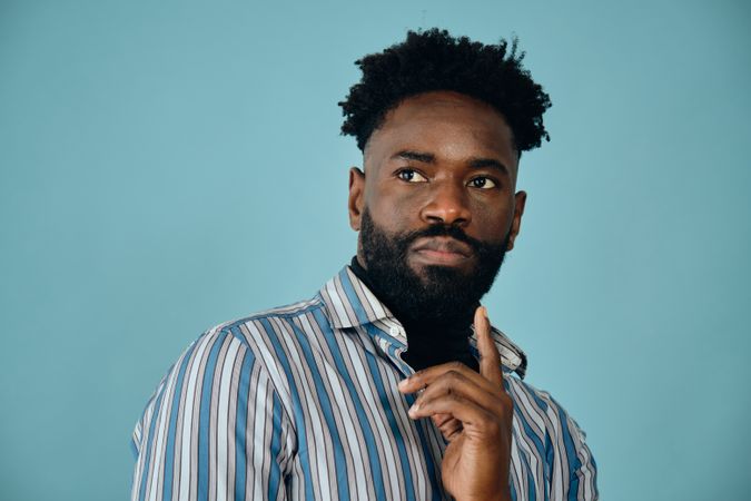 Closeup portrait of a serious Black man in blue studio shoot with finger to chin looking away