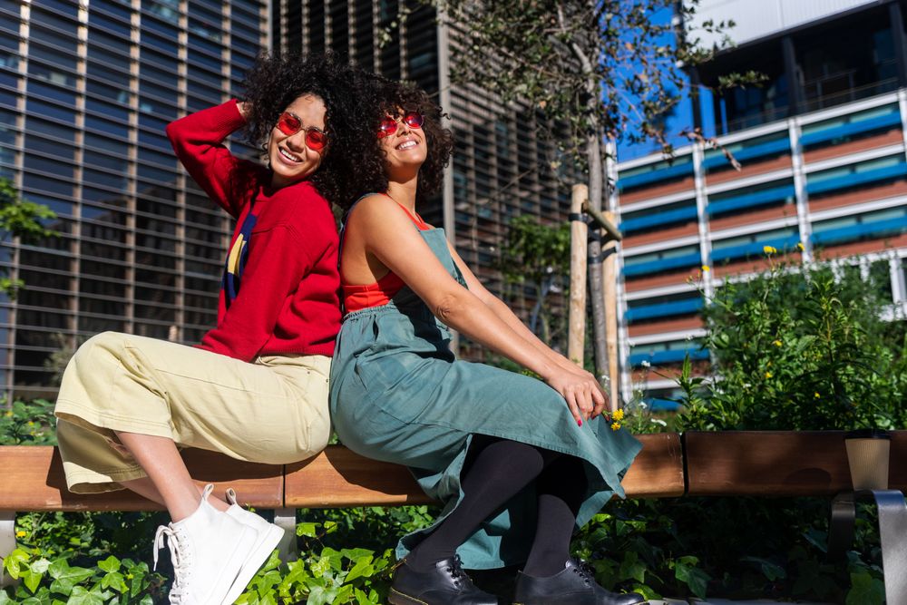 Female friends in fun sunglasses sitting on bench outside