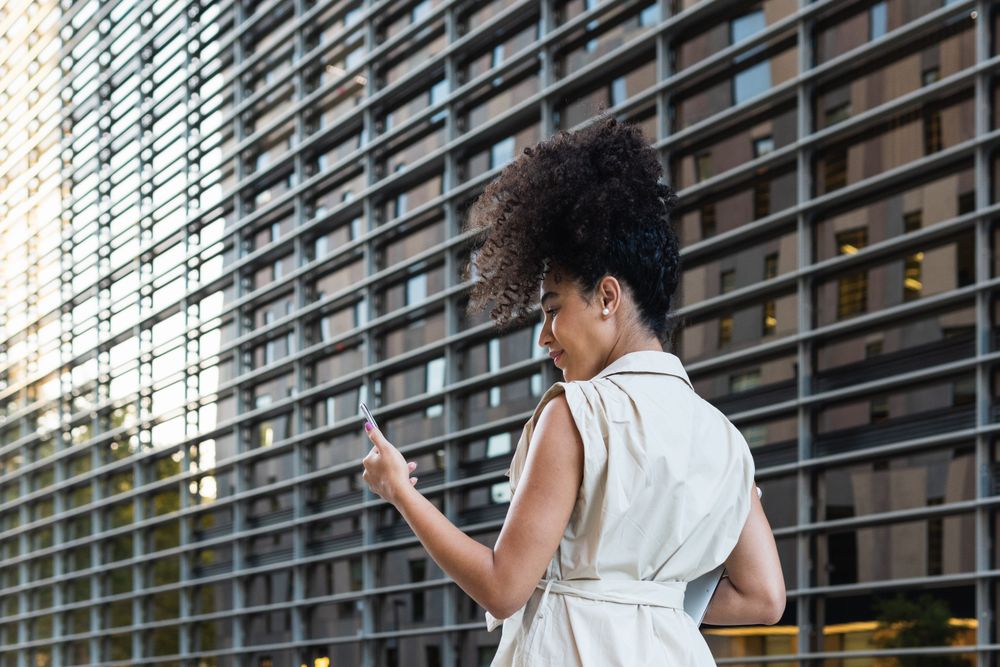 Black woman with laptop checking smartphone