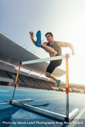 Athlete jumping over an hurdle on running track 0WOxEO