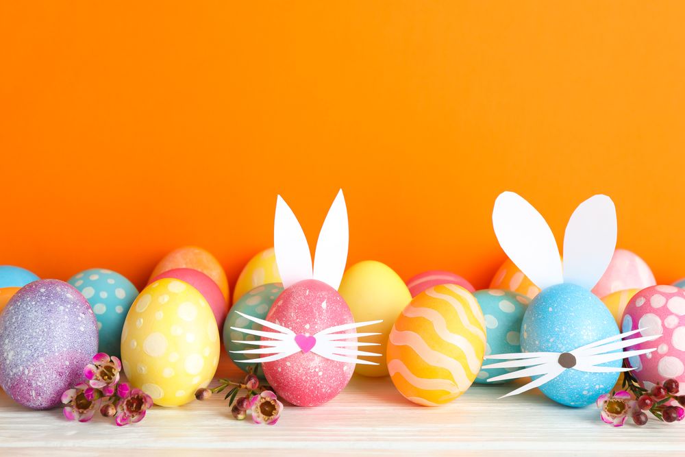 Decorated Easter eggs and cute bunny's ears on table against color background. Space for text