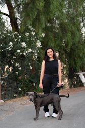 Woman standing in front of green trees on a quiet street with her dog