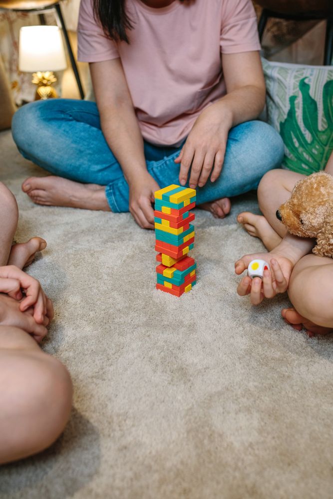 Unrecognizable family having fun making a tower with wooden stacking piece game over carpet at home