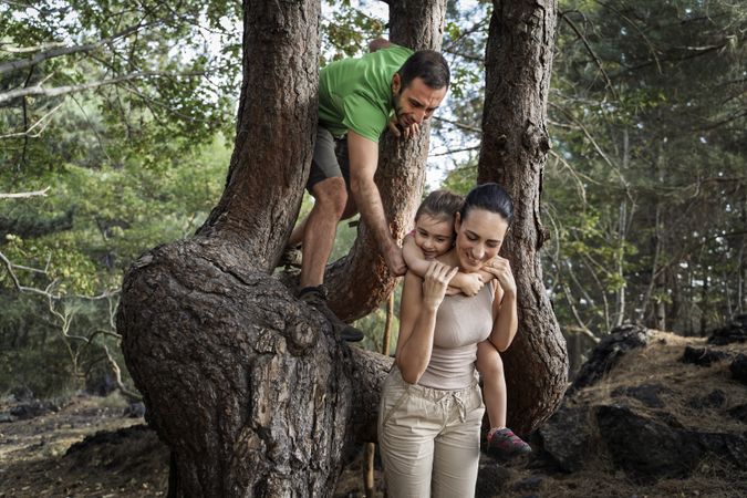 Mother carrying daughter while playing in forest with father climbing tree