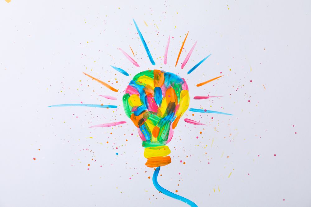 Multicolored light bulb and paint splatters on blank background, space for text
