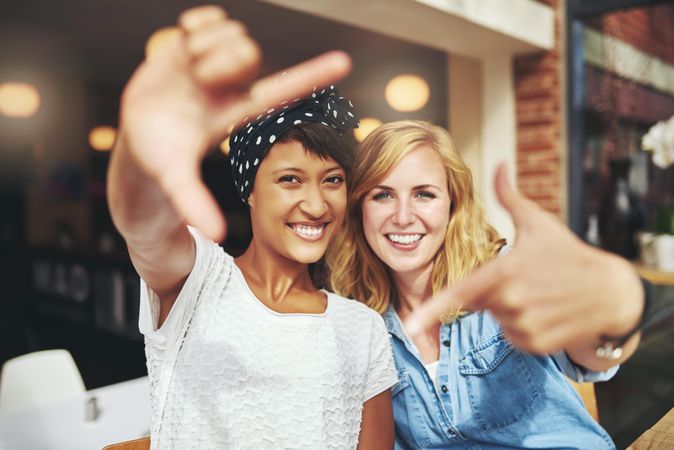 Two smiling women framing their face with their hands in a cafe