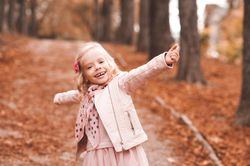 Smiling girl wearing pink jacket standing on autumn fallen leaves