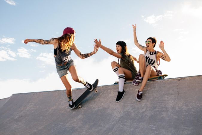 Woman skater giving high five to female friend sitting on ramp during her routine