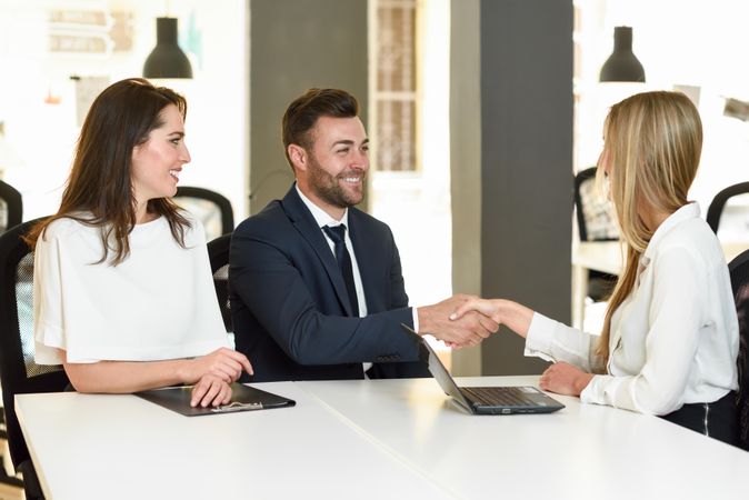 Women and man shaking hands after meeting in bright office