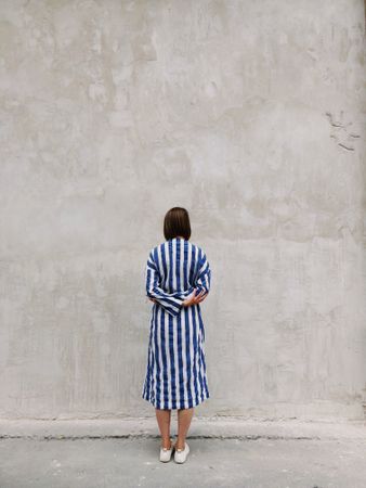 Backside of woman in blue and light dress standing in front of beige wall