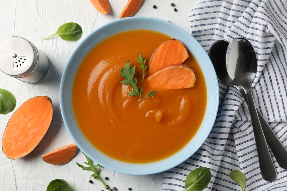Sweet potato soup on table with kitchen towel, salt pepper and spoons