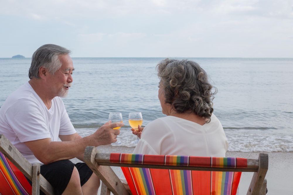 Mature Asian couple relaxing on the beach with wine