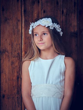 Cute girl in dress and wreath near wooden wall