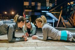 Female sport team doing planks during training in the city at night