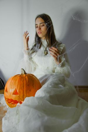 Woman in light dress sitting beside pumpkin indoor