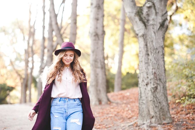 Teenage girl in purple coat with hat walking near fallen autumn tree leaves