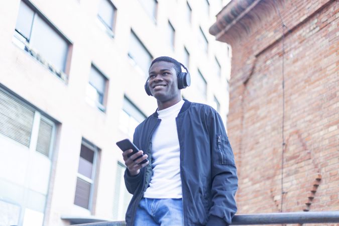 Happy young Black man listening to music on headphones looking down at his phone