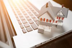 Miniature House And Laptop Computer Resting on Desktop.