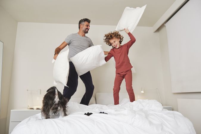 Cheerful man and boy jumping on bed together