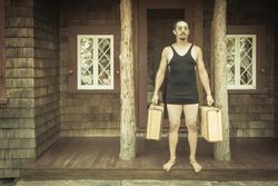 Gentleman Dressed in 1920’s Era Swimsuit Holding Suitcases on Porch