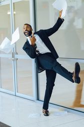 Laughing businessman in suit and tie throwing papers in the air in office