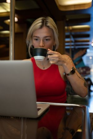 Spanish student with a tattoo works on a laptop and drinks coffee
