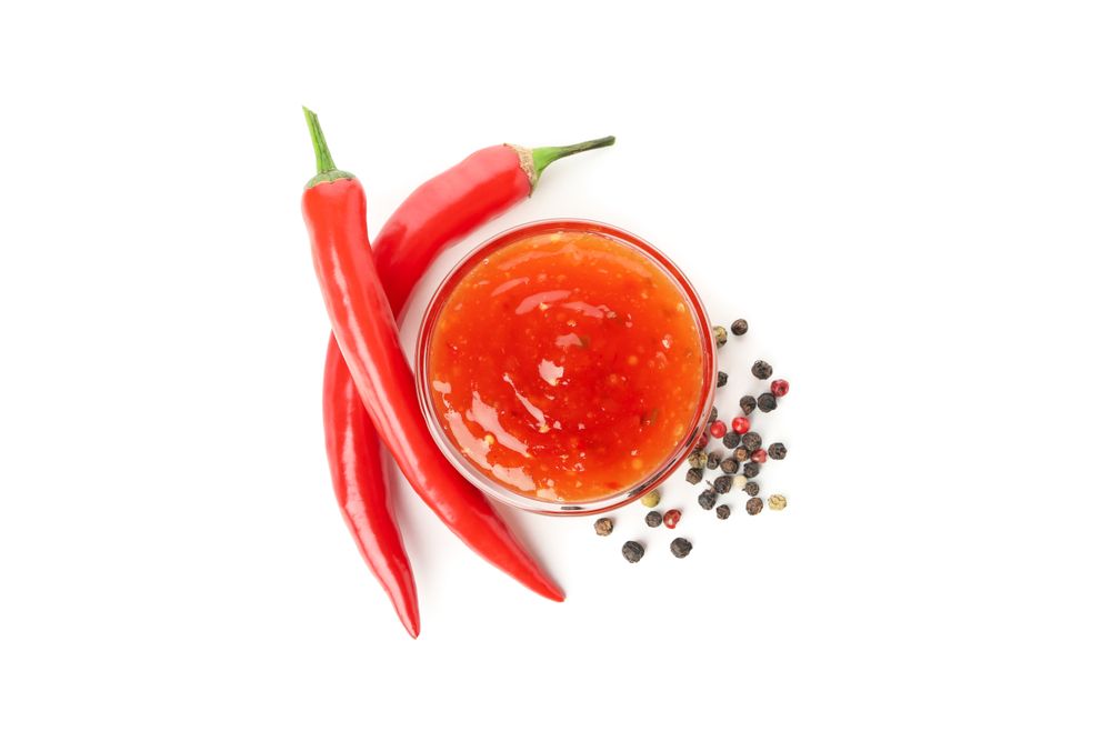 Chilli pepper and bowl of sauce isolated on plain background