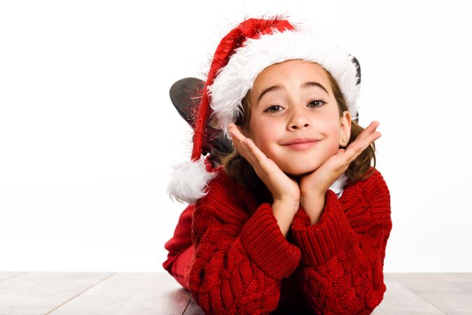 Female child in santa outfit lying on stomach on ground resting her head on her hands