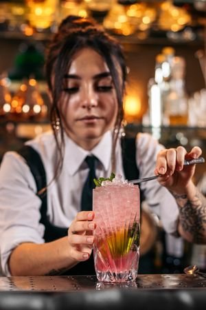 Close-up of a female bartender pouring a cocktail and decorating it with garnish