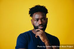 Portrait of Black man contemplating with hand to chin on yellow background 49qdm4